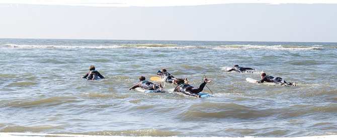 Surfer paddeln auf durch die Wellen der Nordsee bei einem Surfkurs von AllYouCanSurf.