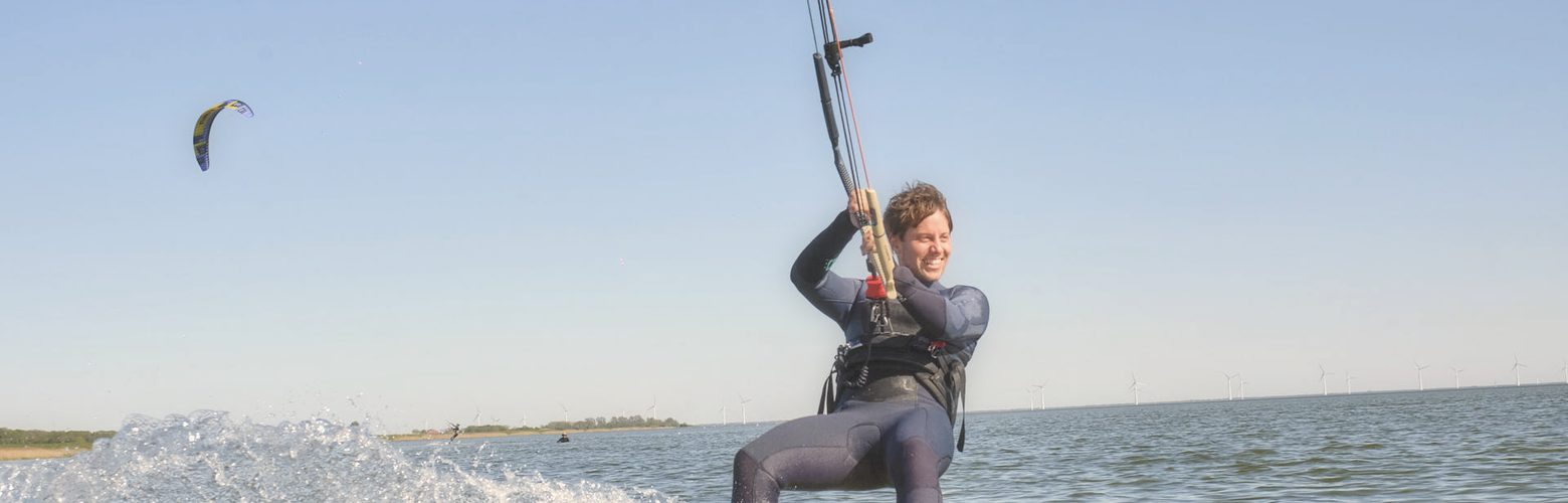Lachende Anfaengerin faehrt auf einem gelben Twintip durch das Stehrevier von Workum am IJsselmeer