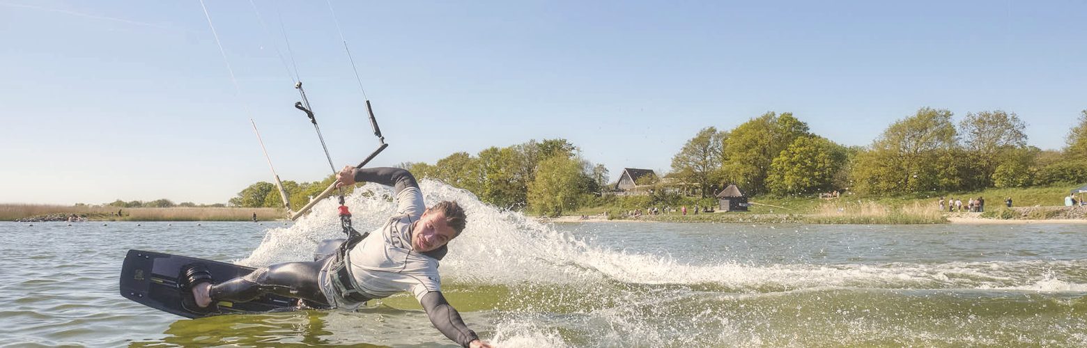 Kitesurfer carvt mit dem Twintip durch das flache IJsselmeer bei Workum, Kite am Himmel