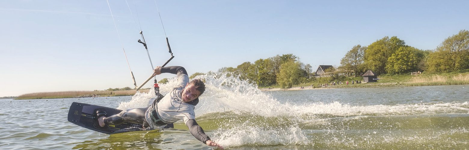 Kitesurfer faehrt mit Spray durch das flache Stehrevier des IJsselmeers bei Workum