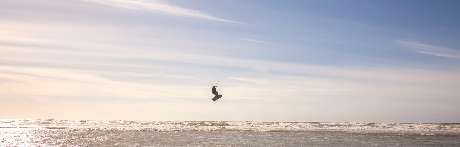 Kitesurfer springt an der Nordsee vor dem endlosen Sandstrand von Petten