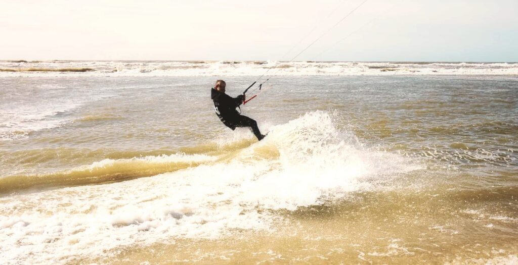 Kitesurfer faehrt in Petten durch die Nordsee-Welle nahe am Strand
